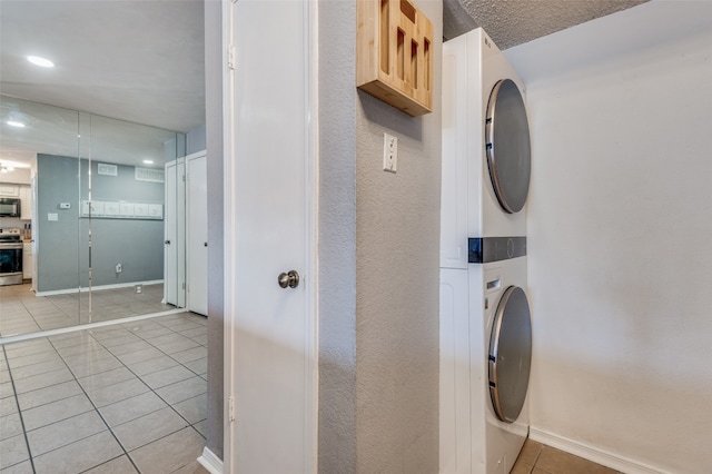 laundry area featuring stacked washer / dryer, a textured ceiling, and light tile floors