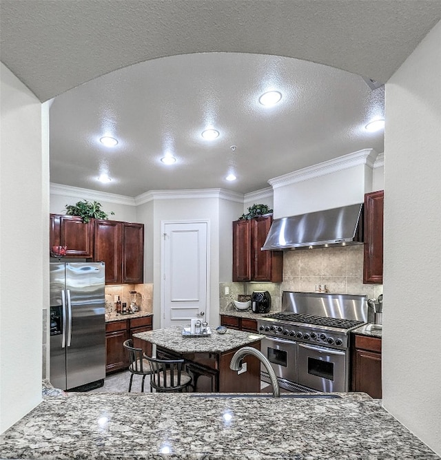 kitchen with stainless steel appliances, dark stone counters, a textured ceiling, tasteful backsplash, and wall chimney exhaust hood