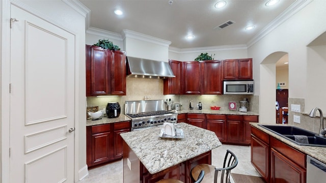 kitchen with light stone counters, stainless steel appliances, backsplash, wall chimney range hood, and sink