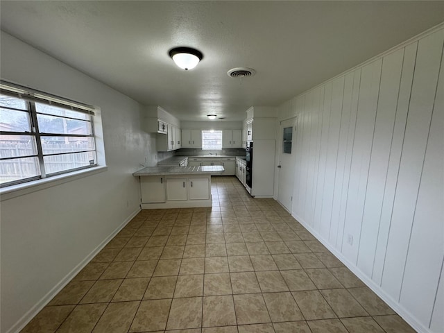 kitchen featuring white cabinets, multiple ovens, light tile floors, and kitchen peninsula