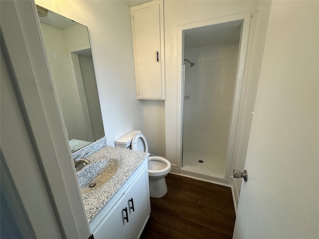 bathroom with wood-type flooring, vanity, toilet, and a tile shower