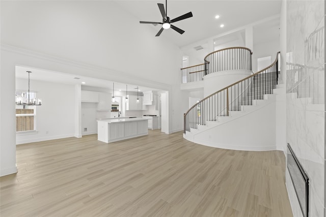 unfurnished living room featuring a towering ceiling, light wood-type flooring, and ceiling fan with notable chandelier