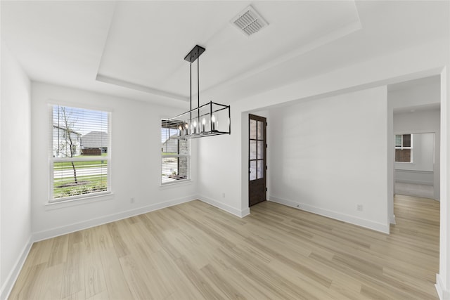 unfurnished dining area with a notable chandelier, light hardwood / wood-style flooring, a wealth of natural light, and a tray ceiling