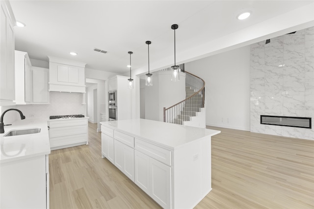 kitchen featuring stainless steel appliances, hanging light fixtures, a center island, sink, and white cabinets