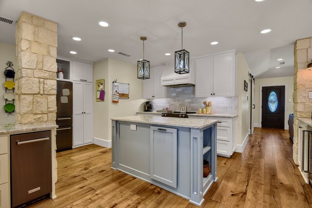 kitchen with light stone countertops, light wood-type flooring, pendant lighting, white cabinets, and a center island