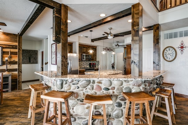 kitchen featuring ceiling fan, stainless steel appliances, decorative light fixtures, a kitchen breakfast bar, and light stone countertops