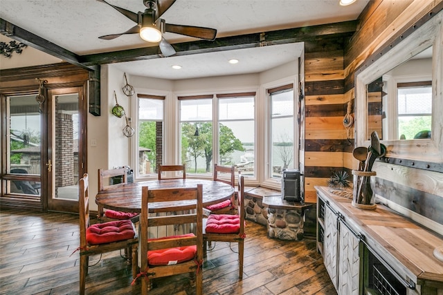 dining space featuring ceiling fan, dark hardwood / wood-style floors, beam ceiling, and wooden walls