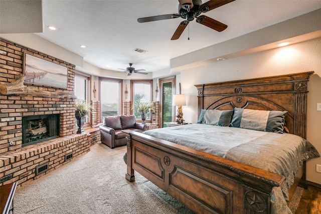 bedroom with a brick fireplace, a textured ceiling, light colored carpet, and ceiling fan