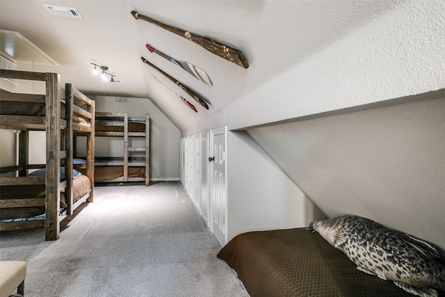 bedroom with light colored carpet, vaulted ceiling, and a textured ceiling