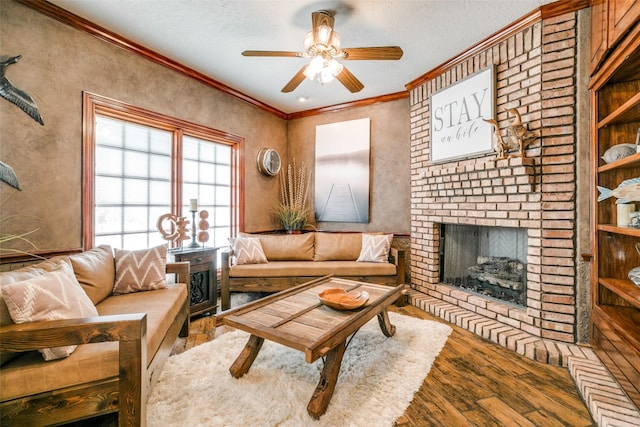 living room featuring hardwood / wood-style floors, ceiling fan, a brick fireplace, a textured ceiling, and crown molding