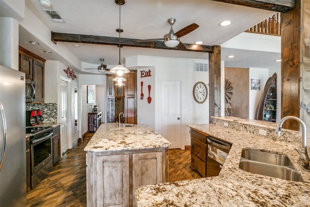 kitchen featuring appliances with stainless steel finishes, hanging light fixtures, ceiling fan, and a kitchen island with sink