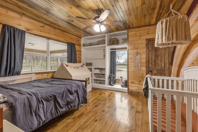 bedroom with wooden ceiling, wood walls, light hardwood / wood-style floors, and multiple windows