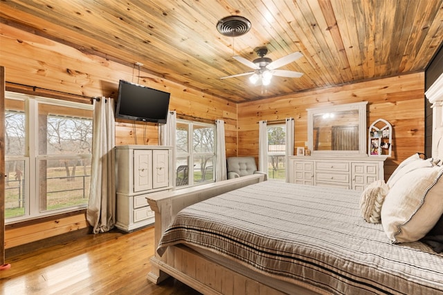 bedroom with wooden walls, multiple windows, and light hardwood / wood-style flooring