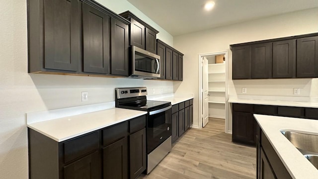 kitchen with sink, dark brown cabinets, light hardwood / wood-style flooring, and appliances with stainless steel finishes