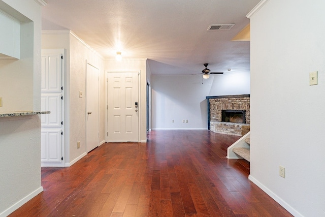 unfurnished living room with ceiling fan, dark hardwood / wood-style flooring, ornamental molding, and a brick fireplace