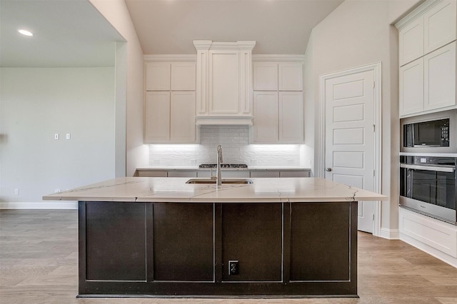 kitchen featuring stainless steel appliances, white cabinets, a center island with sink, and light stone counters