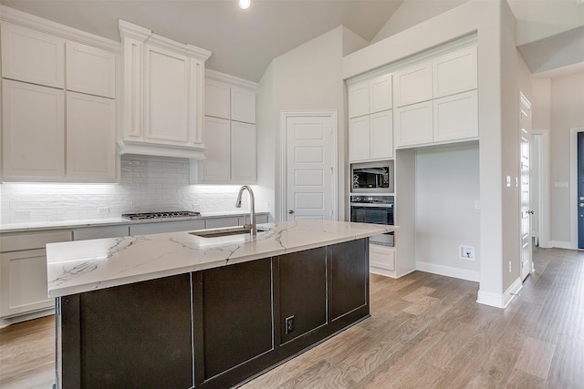 kitchen with lofted ceiling, sink, a kitchen island with sink, white cabinetry, and appliances with stainless steel finishes