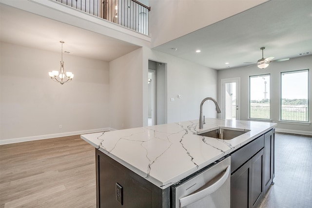 kitchen with dishwasher, light hardwood / wood-style floors, sink, ceiling fan with notable chandelier, and an island with sink