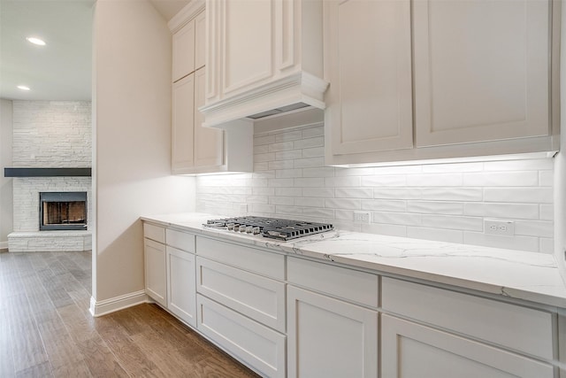 kitchen featuring light stone counters, white cabinets, wood-type flooring, a stone fireplace, and stainless steel gas stovetop