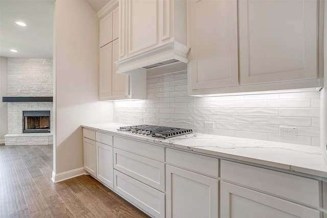 kitchen with light stone counters, a stone fireplace, wood finished floors, white cabinetry, and backsplash