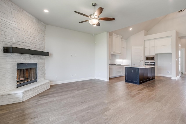 unfurnished living room with a stone fireplace, vaulted ceiling, ceiling fan, and light hardwood / wood-style flooring