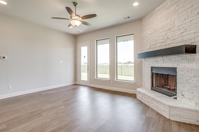 unfurnished living room with wood-type flooring, ceiling fan, and a stone fireplace