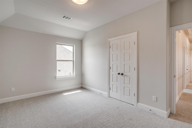 unfurnished bedroom with light carpet, vaulted ceiling, and a closet