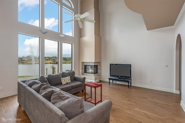 living room featuring a tiled fireplace, ceiling fan, a water view, and light hardwood / wood-style flooring