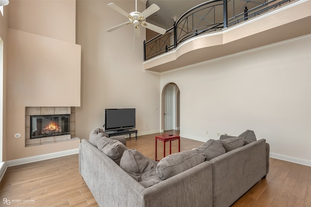 living room with a tiled fireplace, ceiling fan, light hardwood / wood-style flooring, and a high ceiling