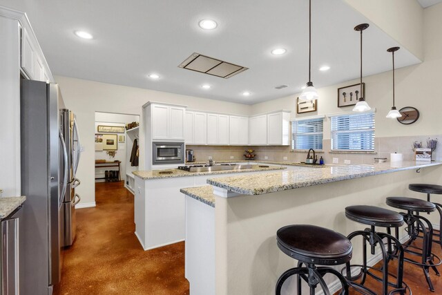 kitchen featuring a kitchen island, light stone countertops, pendant lighting, a breakfast bar, and white cabinetry