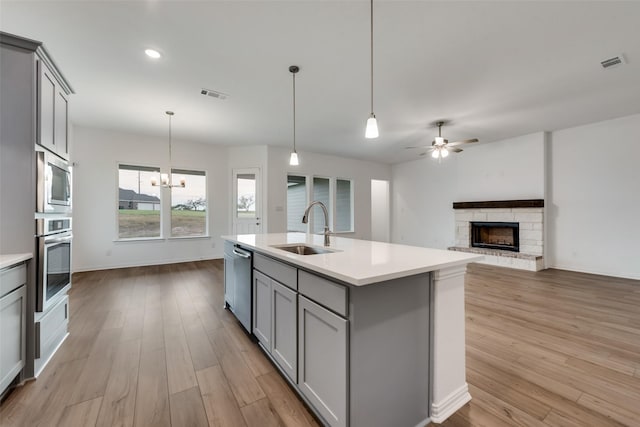 kitchen with gray cabinets, stainless steel appliances, a stone fireplace, and sink