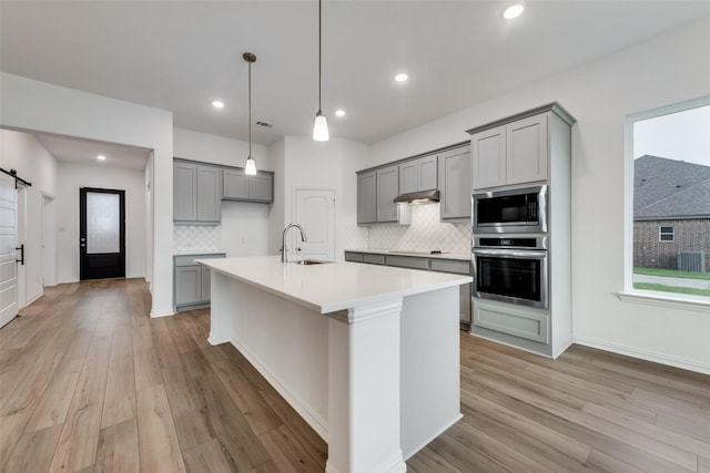 kitchen featuring sink, tasteful backsplash, a barn door, a center island with sink, and appliances with stainless steel finishes