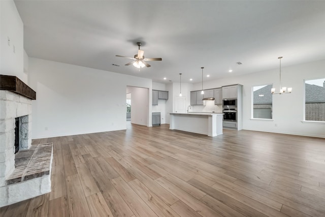 unfurnished living room with ceiling fan with notable chandelier, sink, light wood-type flooring, and a fireplace