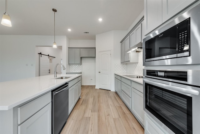 kitchen with decorative backsplash, gray cabinetry, stainless steel appliances, sink, and a barn door