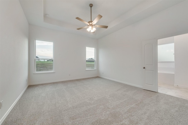 unfurnished room featuring a raised ceiling, ceiling fan, and light colored carpet