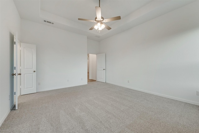 carpeted spare room featuring a tray ceiling, ceiling fan, and a towering ceiling