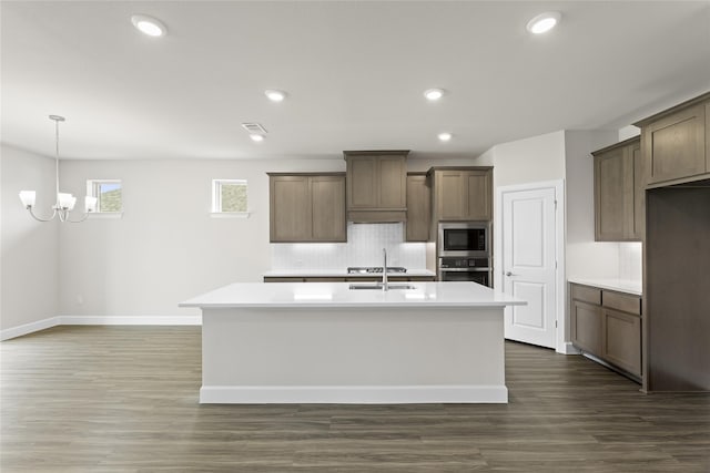 kitchen with a kitchen island with sink, stainless steel appliances, a chandelier, and dark hardwood / wood-style flooring