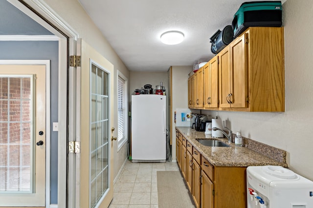 kitchen with white fridge, sink, light stone counters, a textured ceiling, and light tile patterned floors