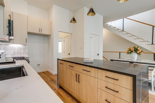 kitchen featuring light wood-type flooring, dark stone counters, light brown cabinetry, hanging light fixtures, and a towering ceiling