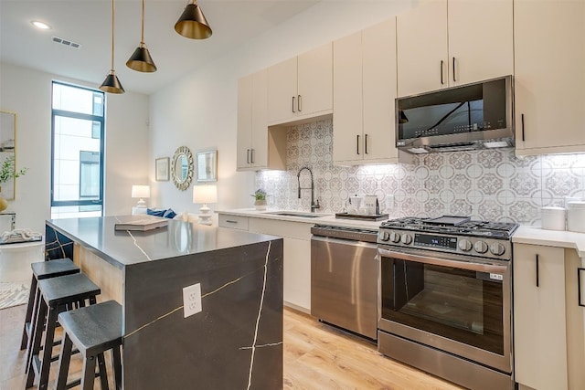 kitchen featuring light hardwood / wood-style flooring, backsplash, appliances with stainless steel finishes, a center island, and sink