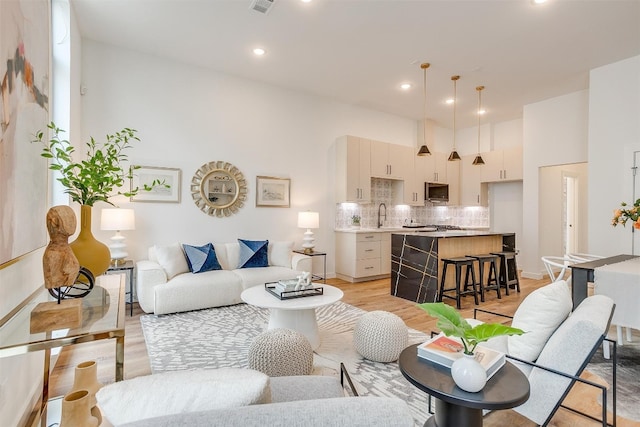 living room with a high ceiling, sink, and light wood-type flooring