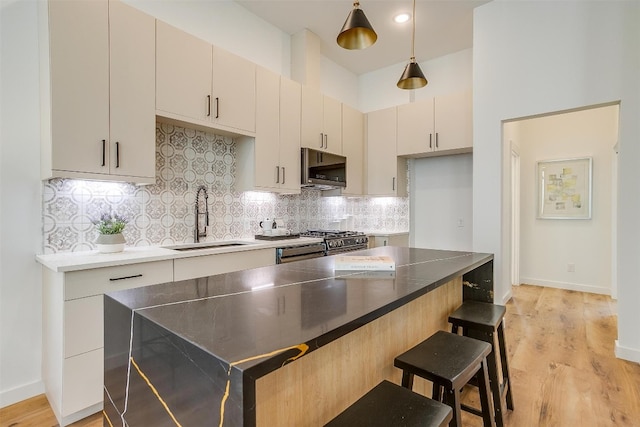 kitchen featuring light wood-type flooring, tasteful backsplash, stainless steel appliances, sink, and hanging light fixtures