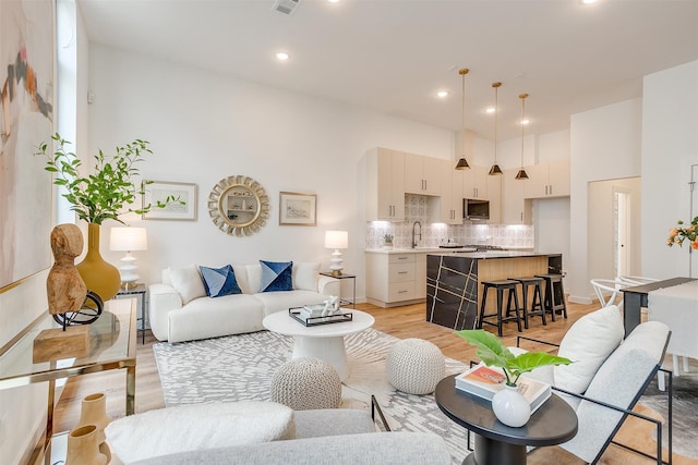 living room featuring a towering ceiling, sink, and light hardwood / wood-style floors