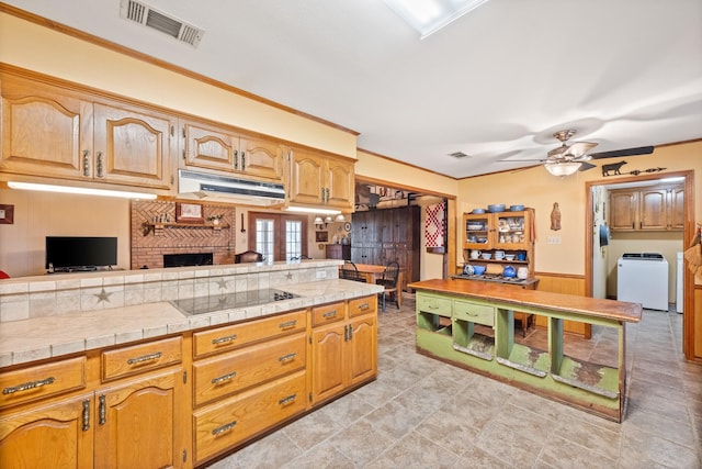 kitchen featuring under cabinet range hood, visible vents, black electric cooktop, and washer / dryer