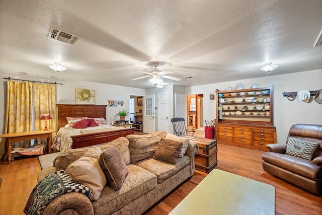 bedroom with a ceiling fan, a textured ceiling, visible vents, and wood finished floors