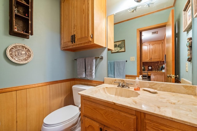 half bathroom with visible vents, toilet, a wainscoted wall, vanity, and wood walls