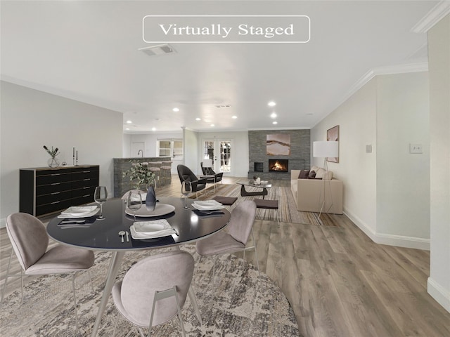 dining space with crown molding, a stone fireplace, light hardwood / wood-style flooring, and french doors