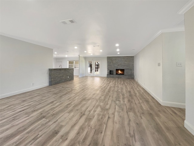 unfurnished living room featuring light hardwood / wood-style floors, crown molding, french doors, and a fireplace