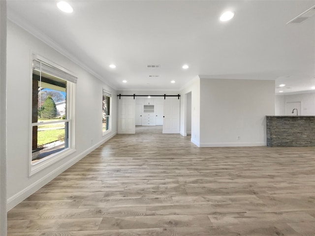 unfurnished living room featuring light hardwood / wood-style floors, crown molding, and a barn door