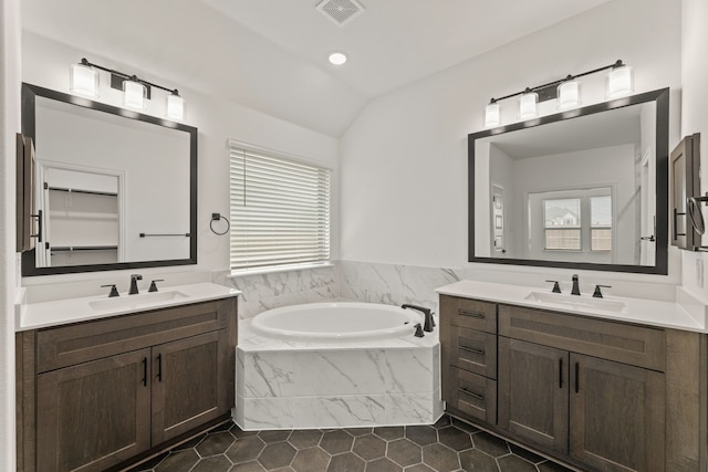 bathroom with plenty of natural light, tiled tub, vaulted ceiling, and vanity